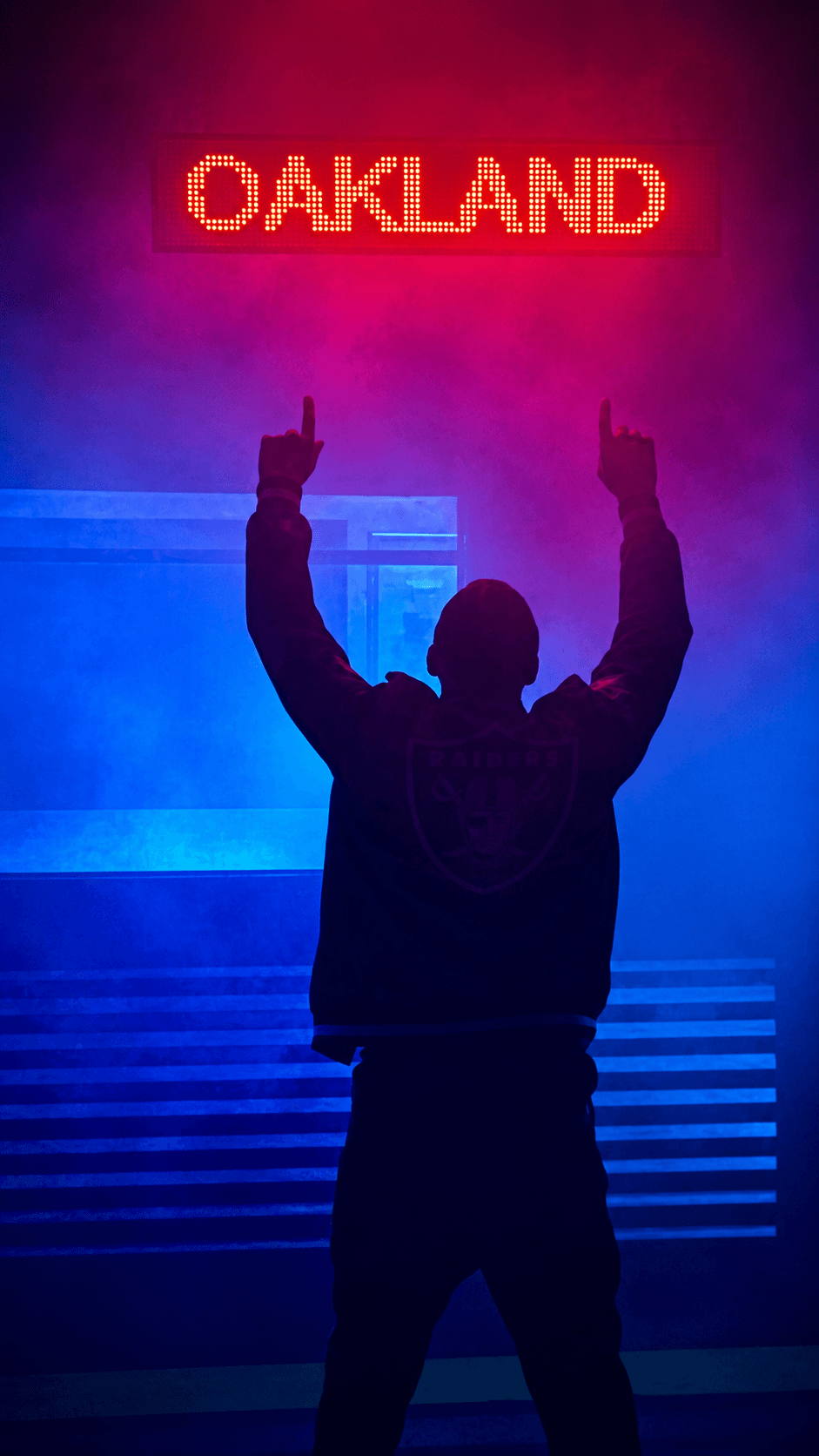 Silhouette with arms raised under a red Oakland neon sign